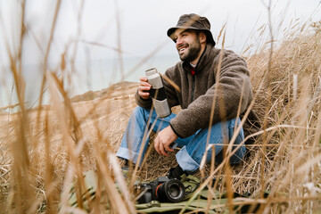 Happy handsome photographer drinking tea while resting outdoors