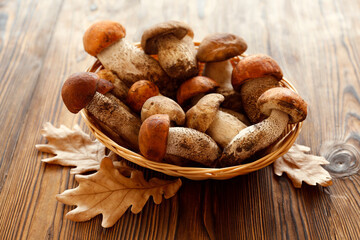 Bunch of porcini mushrooms in small wicker basket on wood textured table. Copy space for text, close up, top view, background.