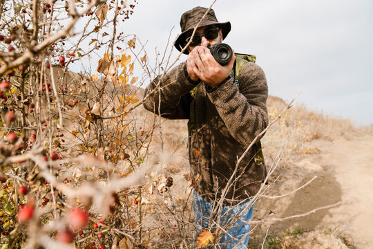 Focused photographer in sunglasses taking photo on digital camera