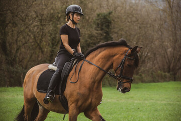 Obraz premium woman riding her brown horse with black mane dressed in black with a helmet