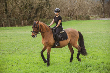woman riding her brown horse with black mane dressed in black with a helmet
