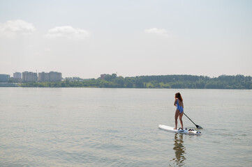 Caucasian woman in a striped swimsuit rides on a SUP board. The girl prefers active rest.