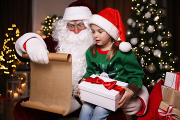 Fototapeta na wymiar Little girl with Christmas gift near Santa Claus indoors