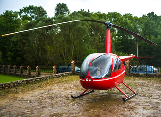 Red small, modern helicopter parked Park. rainy weather.
