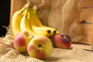 Peaches and bananas, arrangement with Peaches and bananas, rustic wooden box and rustic fabric, selective focus.