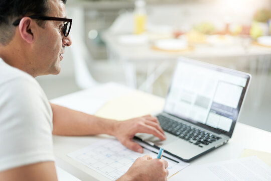 Working even from far away. Close up of focused latin man using his laptop and marking days in calendar while working on the desktop. Work online.