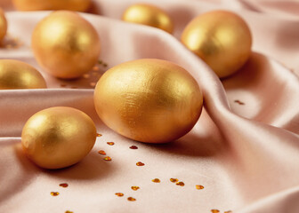 Golden decorative Easter eggs on a background of creamy shiny natural fabric. Soft texture concept. Champagne silk fabric.