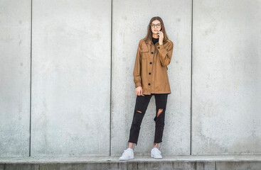 Young girl in glasses speaks by smartphone. student stands on concrete background in the street.
