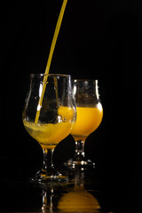 Orange juice, beautiful glasses of orange juice being filled, black background, selective focus.