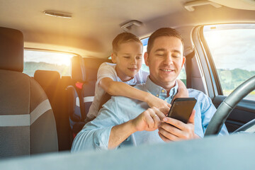 Happy father and son sitting in car and using smartphone in summer sunny day. Happy family travels