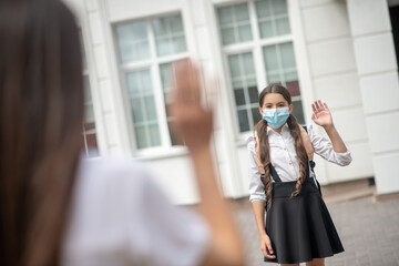 Schoolgirl in protective mask saying goodbye to mom