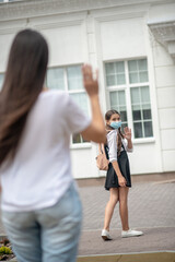 Girl in protective mask near school and mom