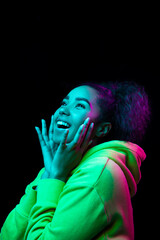 Smiling. African-american woman's portrait isolated on dark studio background in multicolored neon light. Beautiful female model. Concept of human emotions, facial expression, sales, ad, fashion.