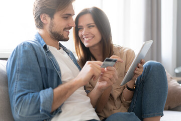Laughing couple sitting on the couch shopping online with tablet pc at home in the living room.