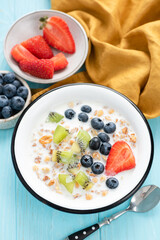 Breakfast cereals with milk and berries blueberry strawberry kiwi in a bowl on blue table