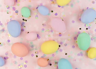 Festive Easter composition. Multicolored pastel Easter eggs and confetti on a pink background.