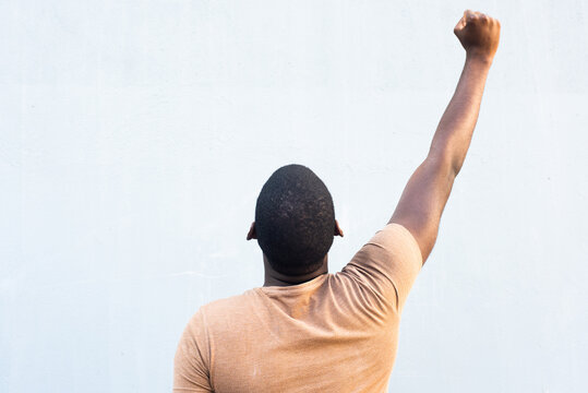 behind young black man with arm raised and fist pump in the air by gray background