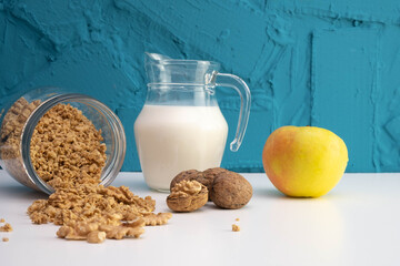 peeled walnuts, a jug of milk and an apple stands next to it