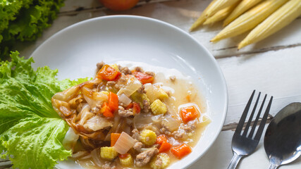 Flate noodle with minced pork sauce on a white plate on a white wooden table with baby corn and tomato and