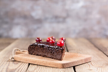 A piece of gluten-free cake in chocolate, decorated with cranberries, on the kitchen board, on a blurry background. Healthy food.