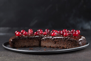 A piece of gluten-free cake in chocolate, decorated with cranberries, on a tray, on a black background. Copy space. Healthy eating.