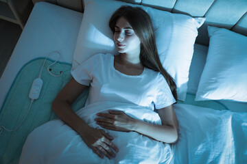Young woman sleeping on electric heating pad in bed at night, top view © New Africa