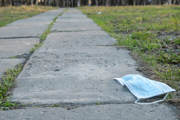 a used, carelessly discarded medical anti virus mask lies on the footpath on the way to the city...