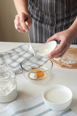 The process of preparing the dough at home. The woman adds the cream cheese to the bowl with the eggs. Vertical photo. Homemade food.