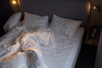 Unmade empty bed in an hotel room. Low light