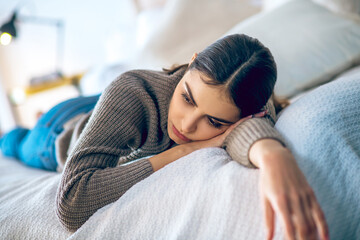 Dark-haired woman lying on bed and looking depressed