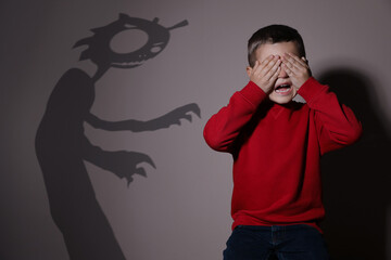Shadow of monster and scared little boy on beige background