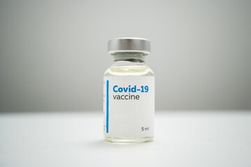 Close up of a COVID-19 vaccine bottle in a clinic. A dose of medical treatment for coronavirus disease in a glass bottle on a white clinic table. Medication for virus infection.