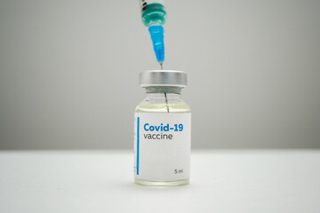 Close up of a COVID-19 vaccine bottle and a syringe for injection. Filling a syringe with a dose of medical treatment for coronavirus disease from a glass bottle on a white clinic table.