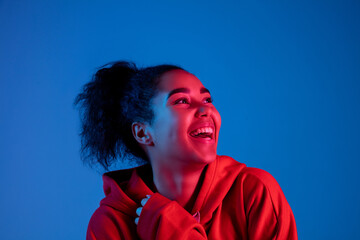 Happiness, cheerful. African-american woman's portrait on blue studio background in red-pink neon...