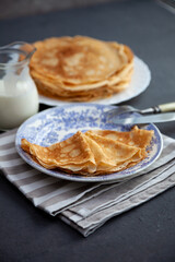 Thin fried pancakes on a plate. Traditional food for Shrovetide. Pancake with sour cream on a wooden table.