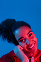 Happiness, cheerful. African-american woman's portrait on blue studio background in red-pink neon light. Beautiful female model. Concept of human emotions, facial expression, sales, ad, fashion.