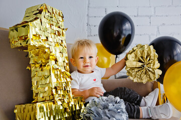 Cute blonde boy on his first birthday at a decorated party in gold, black and silver colors.