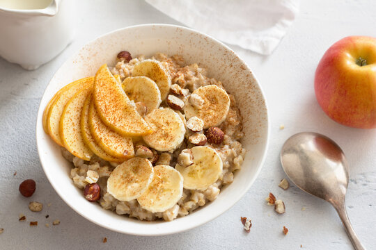 Delicious healthy breakfast. Oatmeal with banana, apple, nuts and cinnamon on a light gray background, top view	
