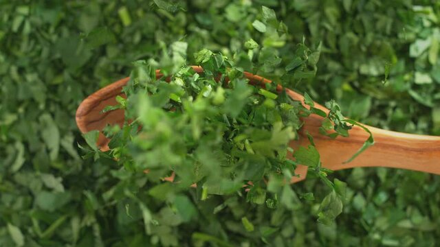 Chopped Parsley on Olive Wood Spoon in Macro Falling onto Green Herbs in Slow Motion