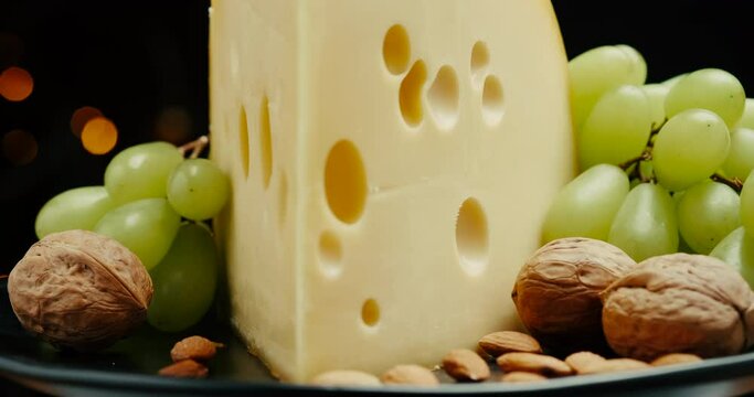 Close up part of Medium hard cheese head edam gouda parmesan on wooden board, with nuts and grapes rotaiting on the plate.