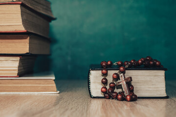 Close up Open Holy Bible and beads crucifix on a red old wooden table. Beautiful green wall background.
