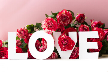 White inscription love against the background of red roses on pink background