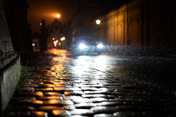Reflections of the paved road through a rainy and snowy night and a headlight of a car