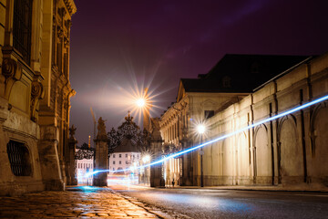 A long exposure of a cyclist driving through a street under an archway at night during a corona curfew