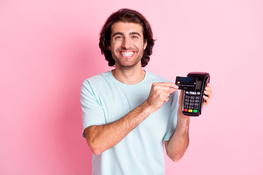 Portrait of optimistic curly hair guy show card terminal wear blue outfit isolated on pastel pink color background