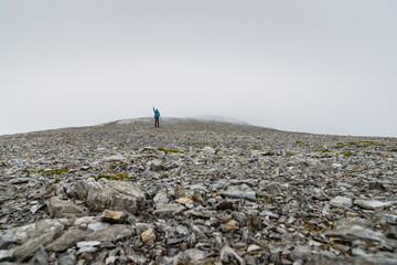 Woman traveler on a mountain plateau in the fog stands in the distance with a raised hand