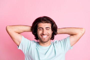 Portrait of charming guy arms behind head closed eyes toothy smile isolated on pastel pink color background