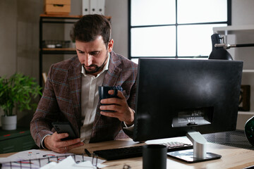 Young businessman working on computer at office. Businessman sitting at office desk drinking coffee and using the phone.