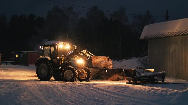 Tractor bulldozer works with lights on the farm at night in winter, snowy