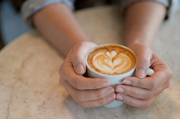 Cropped shot of Hand holding a heart pattern latte coffee cup.